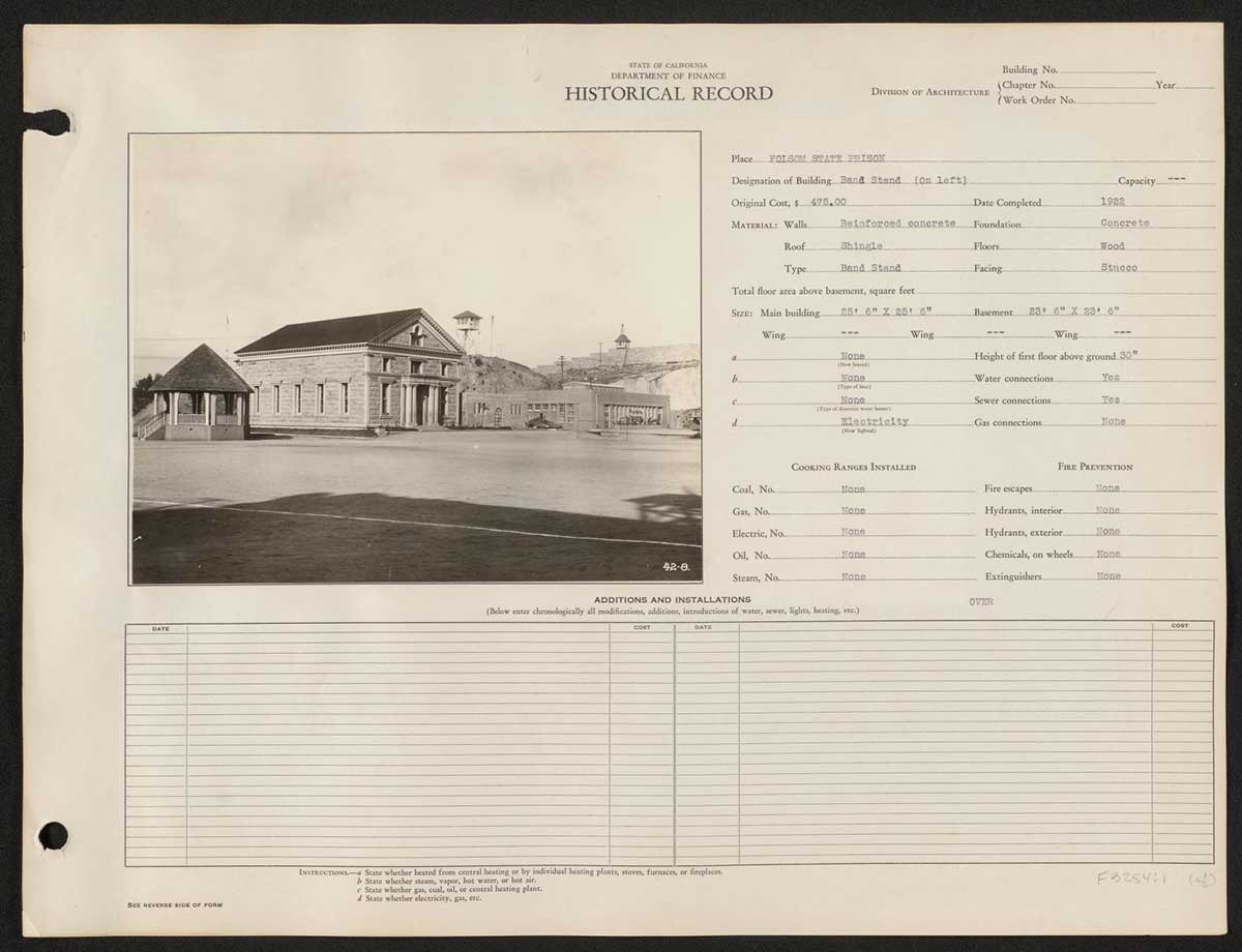 A historical ledger from the California Department of Finance documenting details about Folsom State Prison. The black-and-white photograph shows a large stone building designated as the chapel, completed in 1922 at a cost of $475.00. To the left of the chapel is a small circular structure, identified as the bandstand. To the right, the buildings are designated as the laundry and heating buildings. The ledger notes the building materials, dimensions (25 ft x 25 ft), and various utility connections, such as water and electricity, though it lacks gas connections.