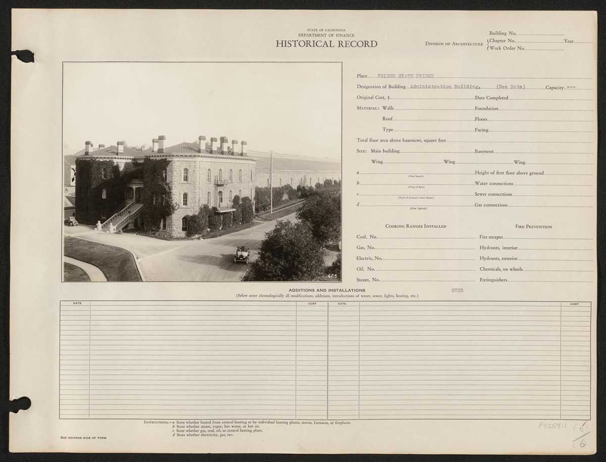 A historical ledger from the California Department of Finance documenting details about the administration building at Folsom State Prison. The black-and-white photograph shows a large stone building covered in ivy, designated as the administration building. The structure features multiple chimneys and a prominent staircase leading to the entrance.  A road and vintage cars are visible in the foreground.